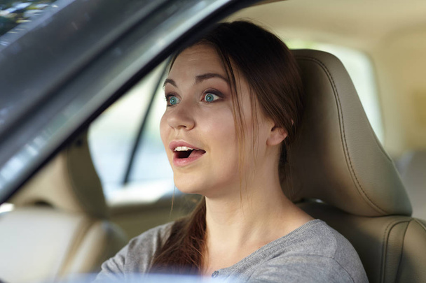 Young attractive caucasian woman behind the wheel driving a car with grimace of astonishment or shock, mouth opened. Strong emotions, wow expression. Copy space. - Fotó, kép