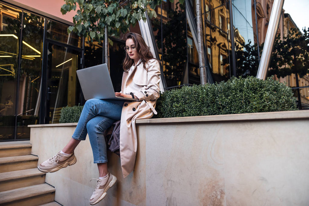 Young attractive businesswoman sitting on the stairs and using modern laptop - Foto, Imagen