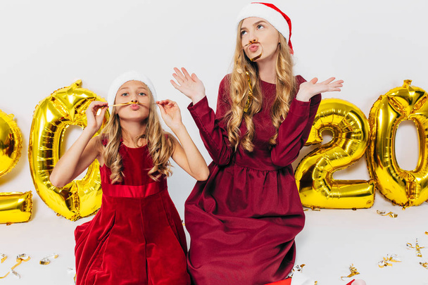 Cheerful mom and her cute daughter in Santa hats. A parent and a - Foto, Imagen