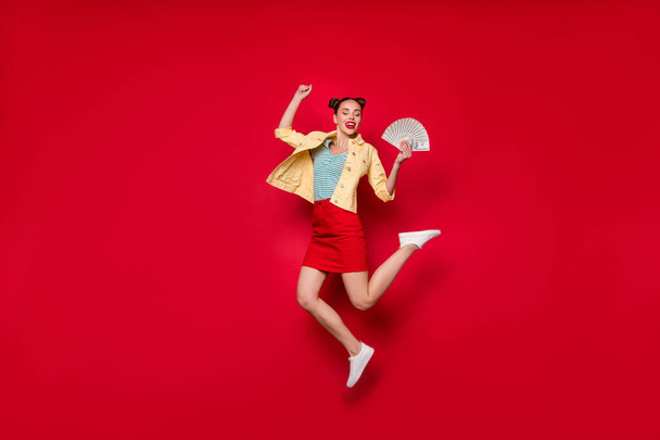 Jumping high overjoyed lady holding fan of bucks hands wear casual outfit isolated red background - Foto, immagini
