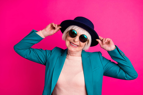 Close-up portrait of her she nice attractive fascinating well-dressed cheerful gray-haired lady touching hat enjoying weekend isolated on bright vivid shine vibrant pink fuchsia color background - Photo, image