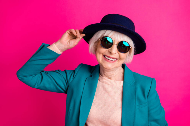 Close-up portrait of her she nice attractive cheerful cheery cool funky gray-haired lady touching hat enjoying life isolated on bright vivid shine vibrant pink fuchsia color background - Фото, зображення