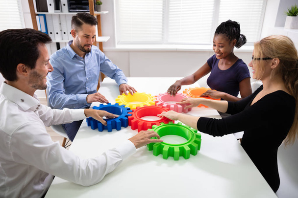 Group Of Businesspeople Arranging Colorful Cog Wheels Together Over White Table At Office - Fotoğraf, Görsel