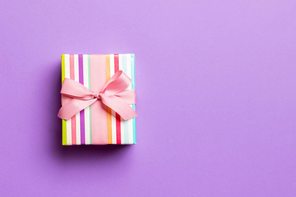 csomagolva karácsony vagy más ünnep kézzel készített ajándék papír rózsaszín szalaggal lila háttér. Jelen doboz, díszítés ajándék színes asztalon, felülnézet másolási hellyel - Fotó, kép
