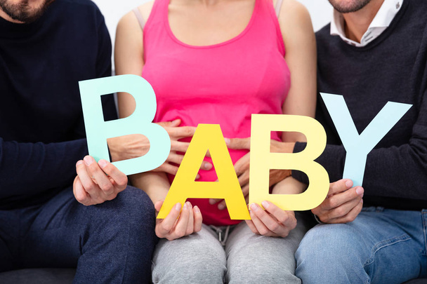 Mid Section Of Male Friends Sitting Together With Her Female Holding Alphabet Of Word Baby - Fotografie, Obrázek