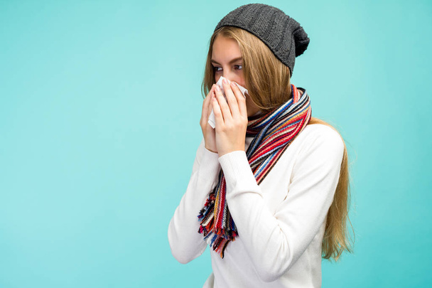 Health and medicine concept - Sad Teen Girl blowing nose into tissue, on a blue background. Pretty girl cold with snot. - Foto, Imagem