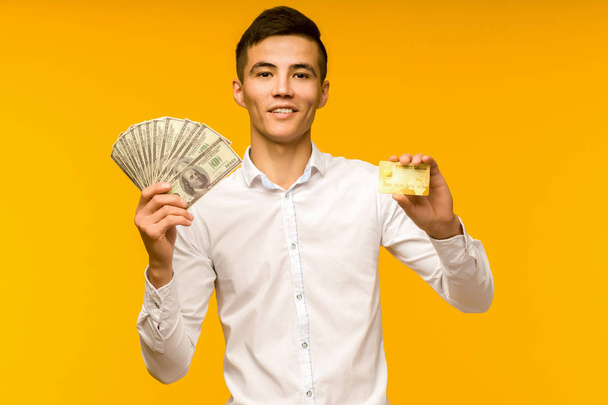 Muotokuva onnellinen nuori aasialainen mies jolla luottokortti ja rahaa kädessä hymyillen ja katsoen kameraa
 - Valokuva, kuva