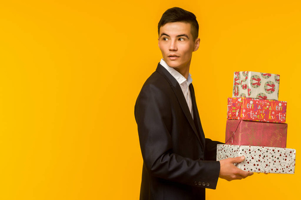 Handsome asian businessman holding gift box over yellow background - Foto, imagen