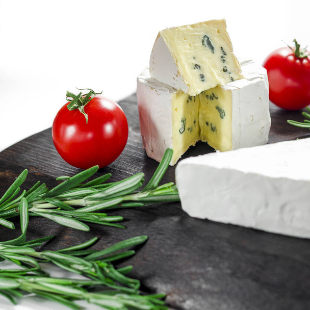 Assorted cheeses on wooden board. Camembert, cheese with blue mildew, mozzarella with tomatoes - Photo, Image