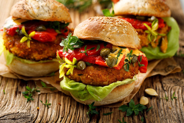Vegan burgery, dýňové burgery s přídavkem grilované papriky, čerstvý salát, aromatické bylinky a kapary na dřevěném venkovském stole, zblízka - Fotografie, Obrázek