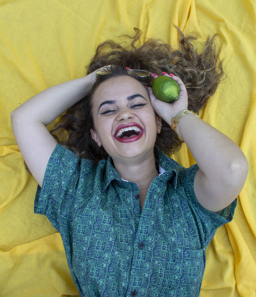 Young woman lying on yellow cloth as background. With curly brown hair. - Foto, Imagen
