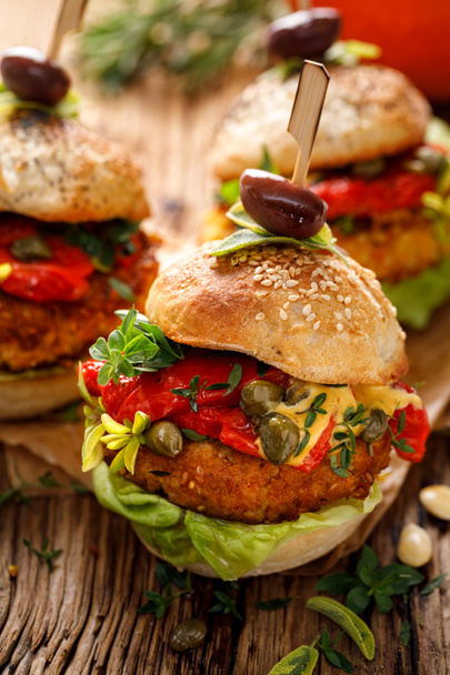 Pumpkin burgers with the addition of grilled peppers, fresh lettuce, herbs and capers on a wooden rustic background, close-up. Vegan burgers - 写真・画像