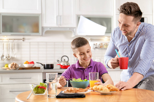 Isä ja poika syömässä aamiaista yhdessä keittiössä
 - Valokuva, kuva
