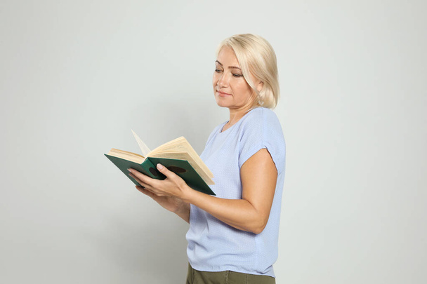 Mature woman reading book on light background - Foto, afbeelding