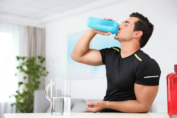 Young athletic man drinking protein shake at home, space for text - Foto, Imagen