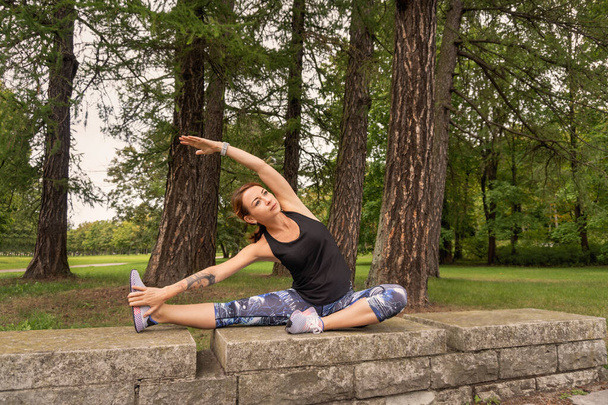 Спортивная женщина в спортивном костюме делает упражнения на растяжку в парке
 - Фото, изображение