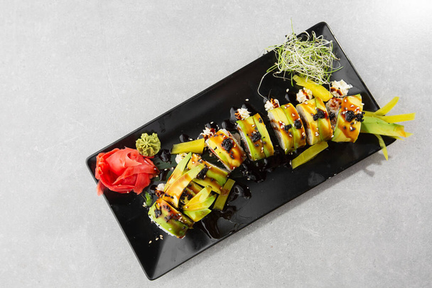 Rouleau de sushi dragon vert avec anguille, concombre, graines de sésame noir et caviar tobiko, nourriture japonaise. Sushi de riz asiatique traditionnel fruits de mer sains. Fond gris. Photo horizontale
. - Photo, image