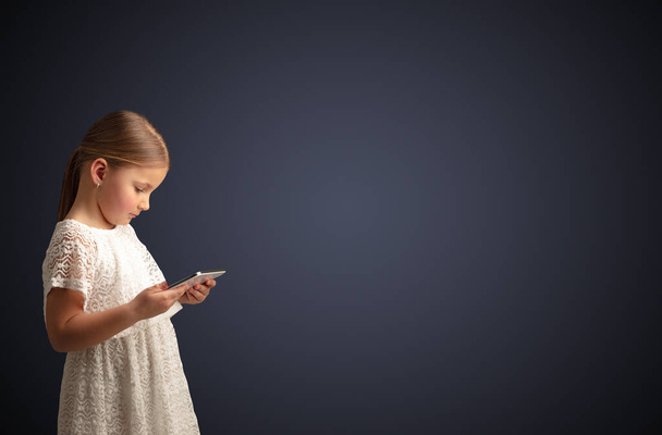 Cute little girl using tablet with dark background - Fotó, kép