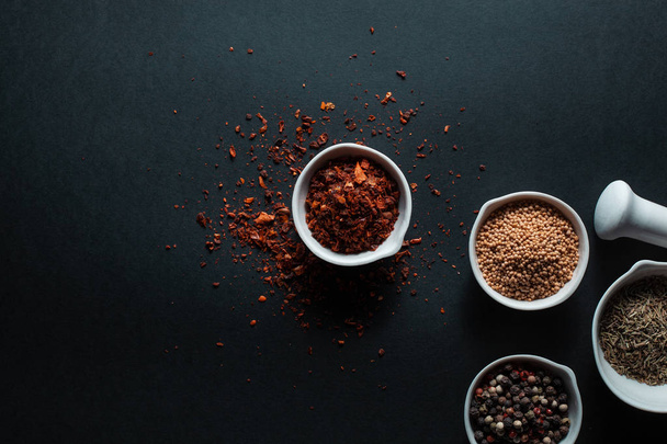 Paprika, mustard, caraway seeds and a mixture of peppercorns in white ceramic bowls next to the mortar isolated on black background - Фото, зображення