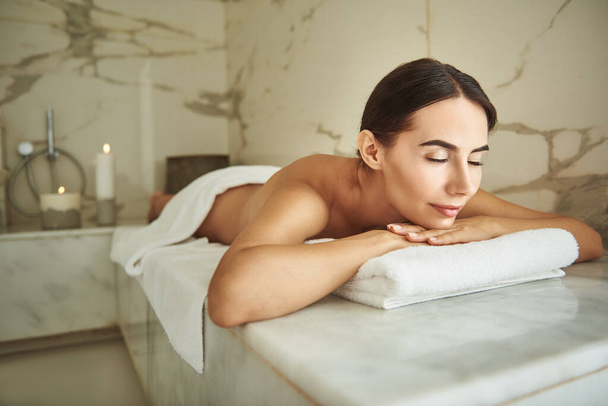 Calm hammam visitor closing her eyes while lying on the white towel - 写真・画像