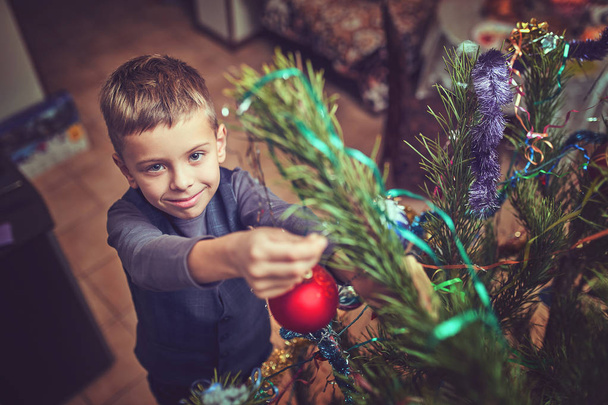 A child decorates a Christmas tree on Christmas Eve in the house - Valokuva, kuva