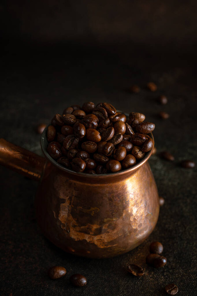 Jezve de cobre con granos de café kopi luwak sobre fondo marrón oscuro, vista de cerca
 - Foto, Imagen
