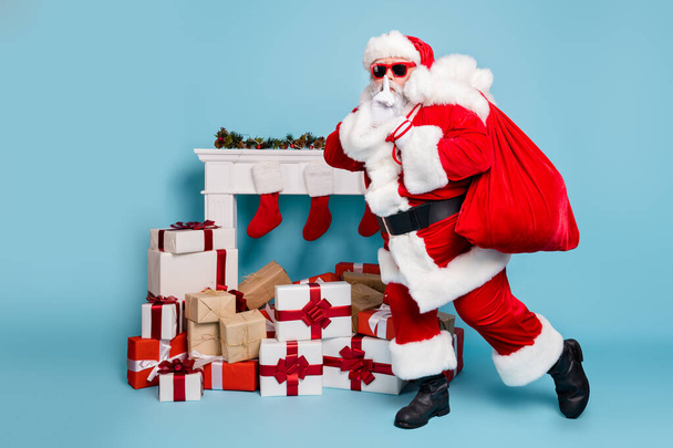 Full length body size view of his he nice fat mysterious bearded Santa carrying delivering big large sack pile stack purchases showing shh sign isolated over blue turquoise pastel color background - Foto, Imagen