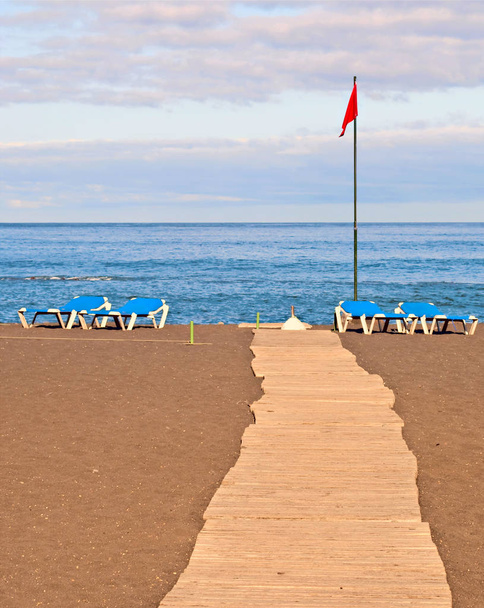 Boardwalk rannalla on useita riippumattoja ja punainen lippu
 - Valokuva, kuva