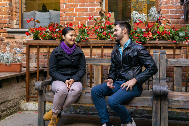 young man and woman talking while sitting on a bench outdoors - Photo, Image