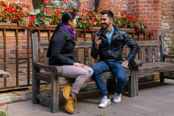 Genç bir adam ve kadın dışarıda bir bankta otururken konuşuyorlar. - Fotoğraf, Görsel