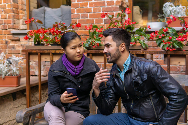 európai fiatalember beszél egy ázsiai lány kezében egy okostelefon - Fotó, kép
