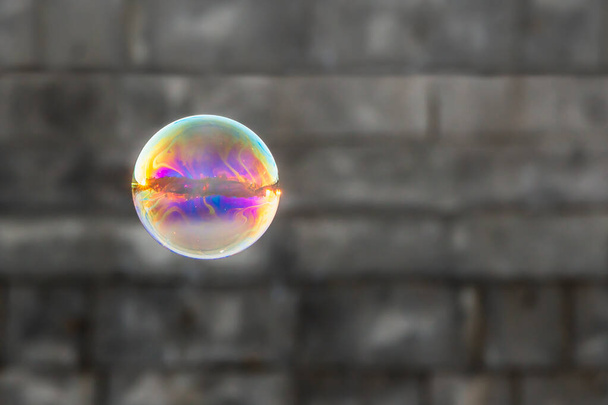 Uma grande bolha de sabão arco-íris no fundo da parede de tijolo cinza borrado
 - Foto, Imagem