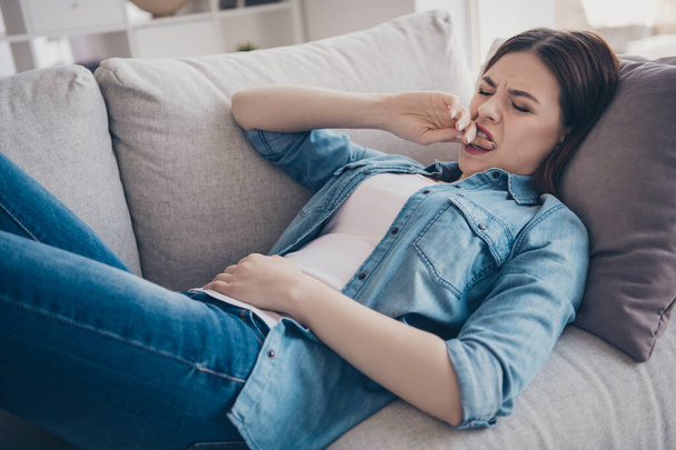 Portrait of stressed depressed woman lying on sofa bite her teeth suffer from terrible stomachache pms needs ambulance wear denim jeans outfit in room - Foto, imagen