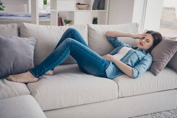 Full size photo of upset depressed girl have sick leave lying on sofa suffer from constipation food poisoning pms wear denim jeans clothes indoors - 写真・画像