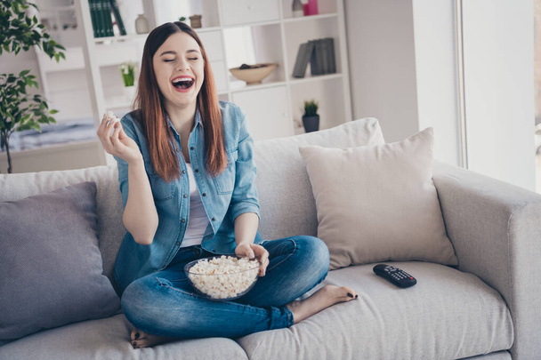 Photo of amazing lady watching favorite humorous tv show eating popcorn laughing out loud sitting comfy sofa wearing jeans clothes apartment indoors - Фото, зображення
