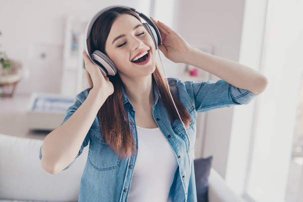 Photo of amazing lady in high spirits listening favorite melody in modern earflaps overjoyed closing eyes wearing jeans clothes apartment indoors - 写真・画像