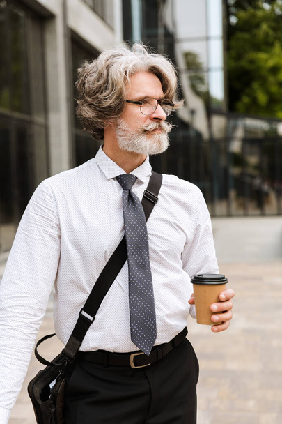Attractive mature businessman wearing suit walking - Фото, изображение