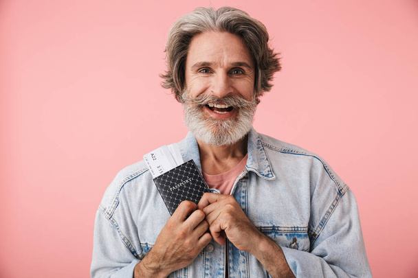 Portrait closeup of joyful old man 70s with gray beard smiling while holding passport and travel ticket - Foto, imagen
