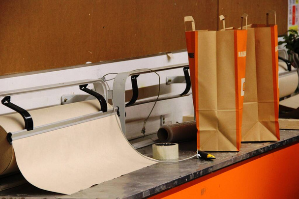 грубая оберточная бумага, клейкая лента, бумажные ножи и пакеты для покупок в гипермаркете, интерьер в оранжевых тонах
 - Фото, изображение