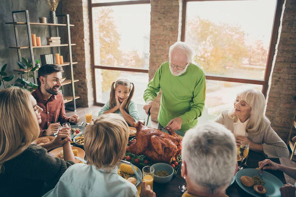 Lets pray. Photo of big family sit feast dishes table around roasted turkey grandfather making slices hungry relatives waiting excited in living room indoors - Фото, зображення