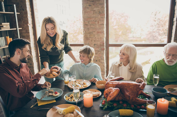 Happy thanksgiving. Photo of big family gathering sit feast meals dinner table wife giving everybody fresh baked bread multi-generation in evening living room indoors - Foto, imagen