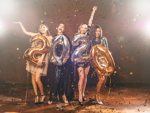 Gyönyörű nők ünneplik az új évet. Boldog Gyönyörű Lányok Stílusos Szexi Party Ruhák Holding Arany és Ezüst 2020 léggömbök, Szórakozás Szilveszter Party. Ünnepi Ünnepség.Kéz felemelése - Fotó, kép