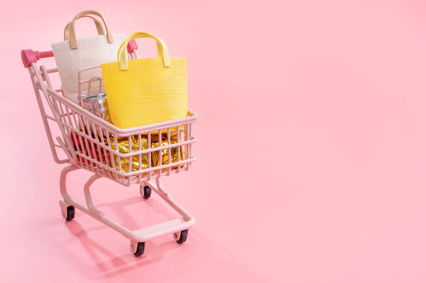 Annual sale shopping season concept - mini red shop cart trolley full of paper bag gift isolated on pale pink background, blank copy space, close up - Fotoğraf, Görsel
