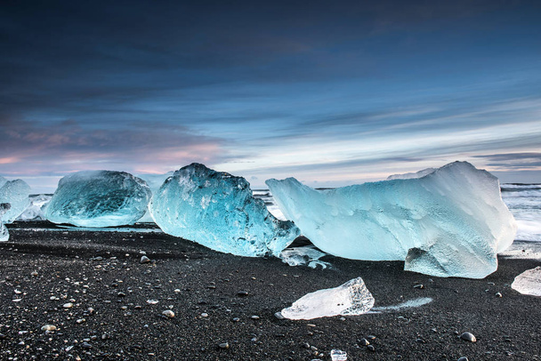 malebný záběr ledovcových kousků tajících na černé písečné pláži na arktickém západu slunce - Fotografie, Obrázek