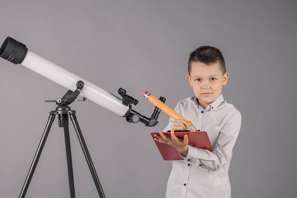jonge astronoom kijkt door een telescoop en schrijft in de tab - Foto, afbeelding