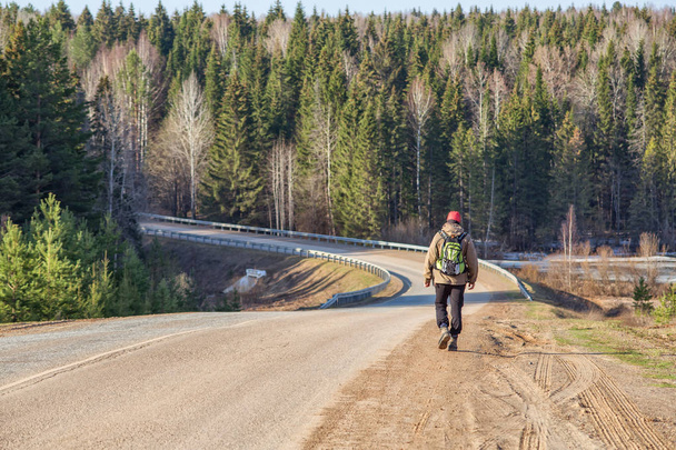 young male backpacker walking on dirt road near forest at sunny spring day  - Foto, imagen