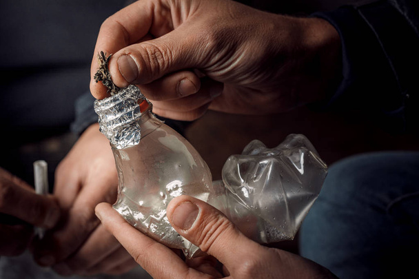 Un uomo fuma droghe attraverso una bottiglia di Bong, un modo di usare il cannabi
 - Foto, immagini