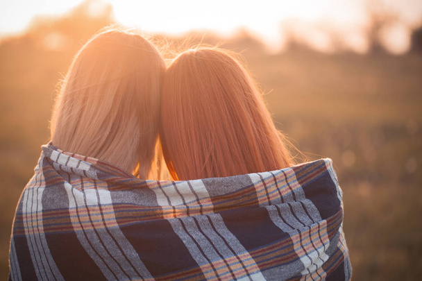 Deux jeunes femmes couvertes d'une couverture regardant le coucher du soleil. Meilleurs amis. Gros plan
 - Photo, image