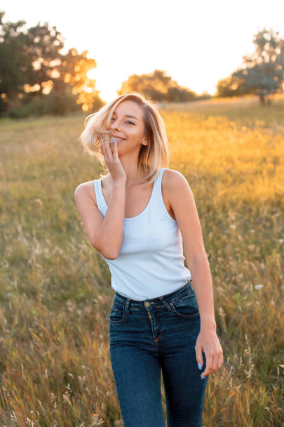 Young woman walking on the field at sunset and smiling - Photo, Image