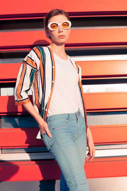 Young fashionable woman in stripe shirt standing on orange background - Foto, afbeelding